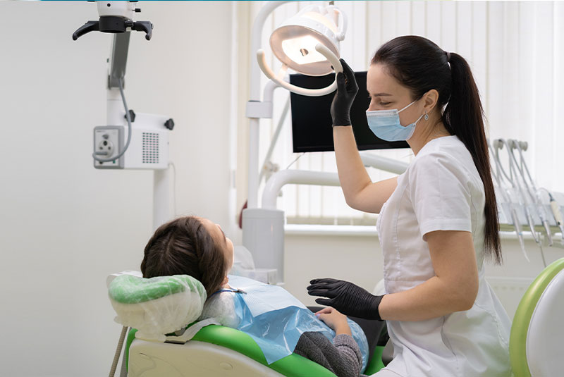 woman dentist doctor in office with dental equipment microscope treats teeth to patient in chair.